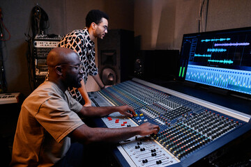 Professional mature African American producer and young musician creating track in recording studio