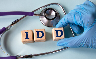 A hand in a medical glove puts cubes with the abbreviation IDD on the background of a stethoscope