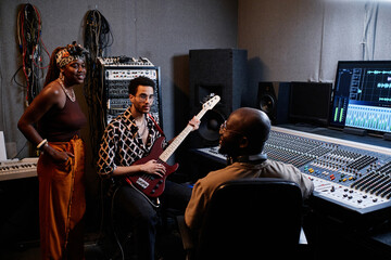 Mature African American music producer and two young musicians discussing something in recording...