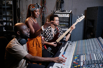 Mature African American music producer, young female singer and male guitarist working on song in...