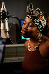 Portrait of modern young African American female singer standing in front of microphone enjoying...