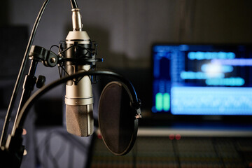 Horizontal no people selective focus shot of microphone with disc pop filter and mixing console in modern recording studio