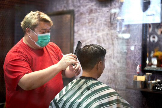 Barber combing the hair of a client while cutting it in a barber shop