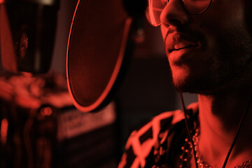Close-up of handsome young Black professional singer recording song in modern studio in red neon...