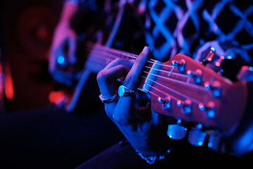 Naklejka premium Medium close-up shot of unrecognizable young male musician playing acoustic guitar in neon light