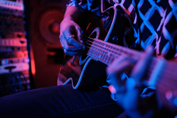 Fototapeta premium Selective focus shot of unrecognizable young male rock musician playing acoustic guitar in studio, neon lighting