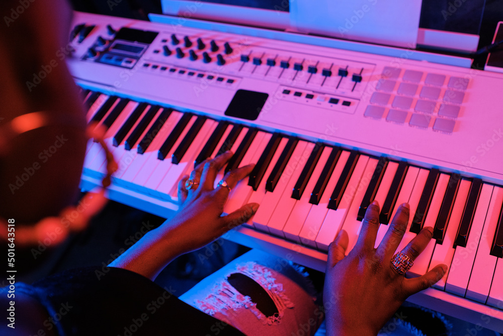 Wall mural High angle view of unrecognizable young Black woman playing synthesizer in recording studio in neon light