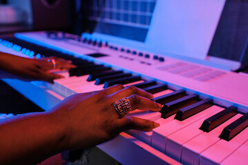 Close-up of unrecognizable Black womans hands playing electronic keyboard in blue and pink neon light