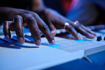 Unrecognizable young Black female musicians hands pressing buttons adjusting sound settings of digital keyboard