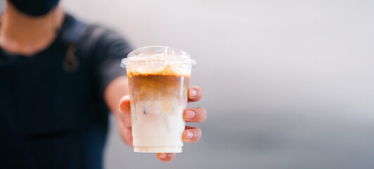 Cold brewed iced latte coffee, Ice coffee latte cup in a plastic glass on. barista hand in coffee cafe.banner background.Cold brew coffee ads.Latte with milk caffeine.plastic ice cup.Arabica roasted.
