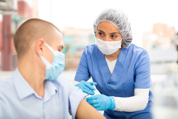 Professional female nurse injecting vaccine in shoulder of male patient during covid vaccination in...