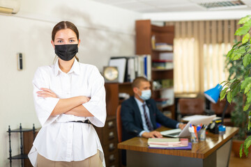 Portrait of a young female employee wearing a protective mask standing in a well-lit office of a large company ..during a pandemic. Close-up portrait