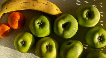 Bananas, tangerines and apples in a fruit basket. Fruits in white basket under sun light