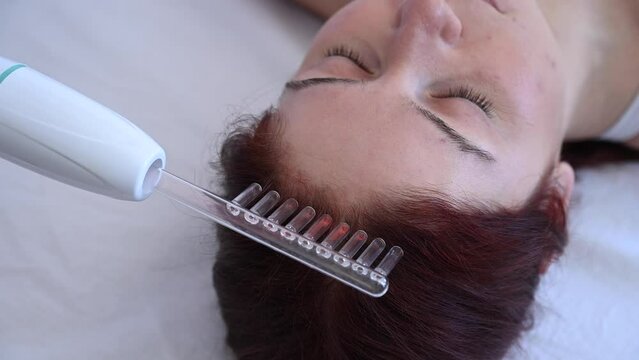Caucasian woman on a hair care procedure using the Darsonval apparatus.