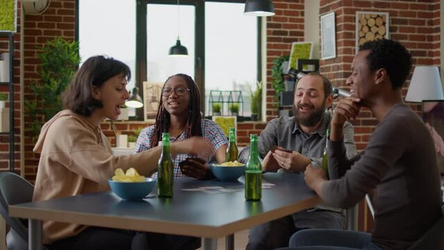 Happy group of people enjoying board strategy with cards and dice, having fun with modern competitive game at home. Men and women playing party games activity for entertainment.