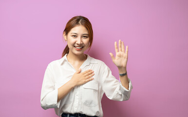 Optimistic, honest and cute asian girl give oath, swear tell truth, put hand on heart and raise one arm as making promise, express devotion and declare telling only truth, stand pink background. - obrazy, fototapety, plakaty