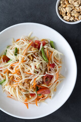 Papaya salad in a white bowl on a dark background, close-up. Thai food top view.