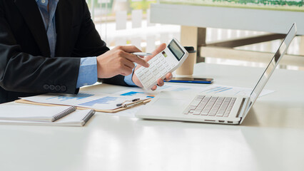 Close-up of a financial businessman hand pressing a white calculator to calculate numbers from...