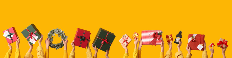 Many hands with Christmas gifts and decorations on yellow background