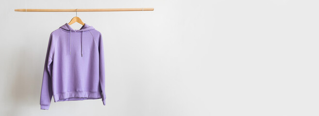 Modern hoodie hanging on light background with space for text