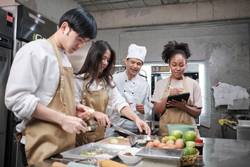 Hobby cuisine course, senior male chef in cook uniform teaches young cooking class students to peel...