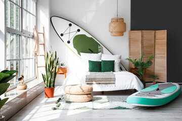 Stylish interior of bedroom with boards for sup surfing near light wall