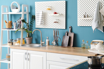 Wooden counter with silver sink, pegboards and shelving unit near blue wall in kitchen