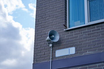 Megaphone hanging on apartment building. City hazard warning system. Loud speaker on brick wall...