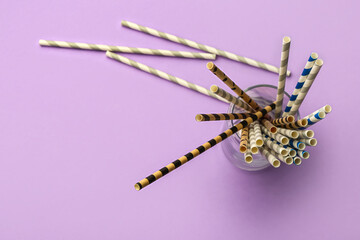 Glass with stylish straws for drinks on purple background