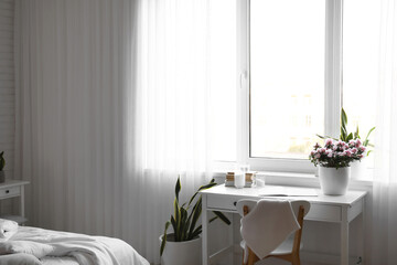 Comfortable workplace with beautiful begonia flowers near window in light bedroom