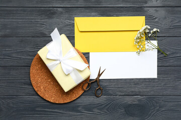 Envelope with blank card, flowers, scissors and gift on dark wooden background