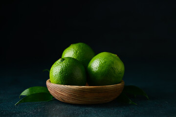 Wooden bowl of fresh limes on dark background