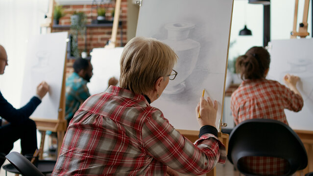 Old woman drawing model with artistic technique on canvas, learning to draw vase at art class lesson. Senior person attending workshop to practice creative skills as new years resolutions.