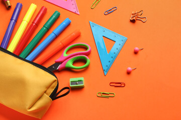 Pencil case with school stationery on orange background