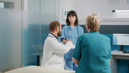 Obraz premium Patient in retirement age signing checkup files in office, after attending consultation appointment with doctor. Health specialist having conversation with old woman about recovery.