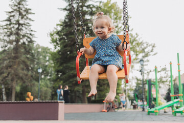 sweet baby in a blue dress swings on a swing on a playground in the park. lifestyle