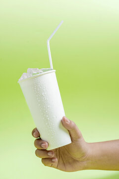 Human Hand Holding A White Plastic Cup With Ice Cubes And A Straw