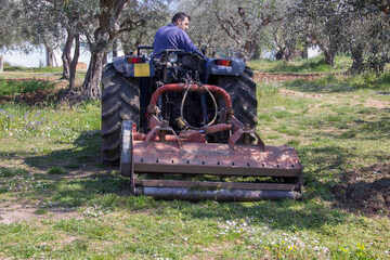 Obraz premium Man on a tractor in a field cutting the grass with a flail mower. You work in the countryside