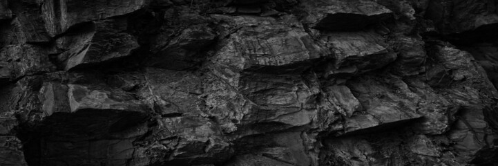 Black white rock texture. Rough mountain surface. Close-up. Volumetric stone background with space for design. Dark gray grunge backdrop. Wide banner. Panoramic.
