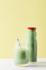 healthy green smoothie in glass, bottle with straw on yellow background. Vegetarian healthy lifestyle concept.refreshing drink. quick snack.copy space