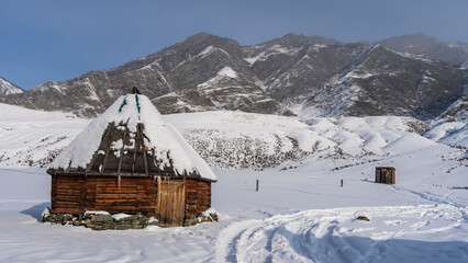 The old wooden hexagonal Altai house - ail in a snow-covered valley. Icicles hang from the conical...