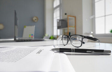 Closeup of pen and glasses with paper agreement for signing lay on table in office. Focus on...