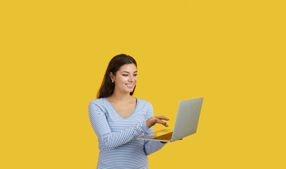 Naklejka premium Happy woman with laptop making presentation, working, shopping online or corresponding with friends. Smiling caucasian brunette woman with laptop isolated on vivid yellow background. Online concept.