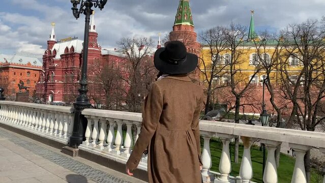 Young beautiful lady elegance madame in hat and coat walking on Red Square  near Historical Museum, Kremlin, Alexander Garden and Okhotny Ryad. Spring, blooming flowers. Center of Moscow, Russia.
