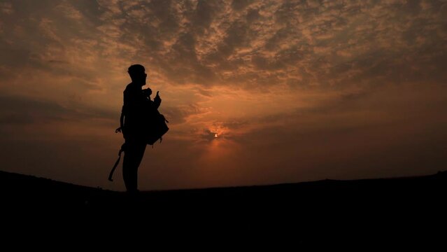 Silhouette shot of an Indian hiker removing his backpack after reaching the peak of mountain. Hiker takes off his bag after reaching the summit. Hiker relaxes after reaching at the peak. 