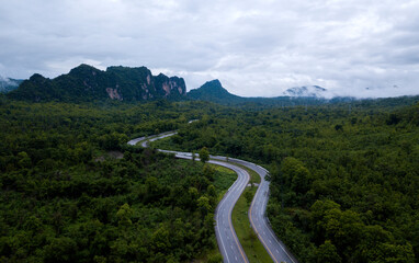 Fototapeta na wymiar Top view of countryside road passing through the green forrest and mountain
