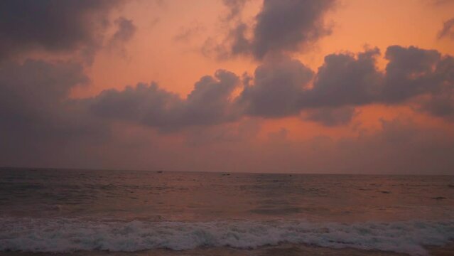 Wide angle slow motion shot of sea waves during the sunset at Colva Beach in Goa, India. Clouds above the sea during the sunset. Beautiful beach sunset background. Summer holidays at beach concept.
