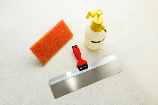 Paint set: spatula, liquid sprayer and grater cleaning tiles with a sponge on the concrete floor. Repair tools lies on floor