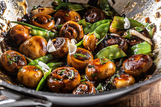 Roasted mushrooms in a wok with spring peas, onion and teriyaky sauce