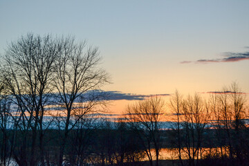 Natural landscape at sunset time on the shore of the lake with dark silhouettes of trees, colorful sky and reflection in the water